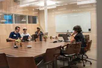 Four at a conference table with laptops