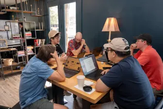 Four at a table with laptops, a lamp behind